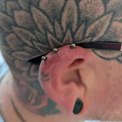 Side view of a heavily tattooed man's head, showing a triple helix ear piercing.