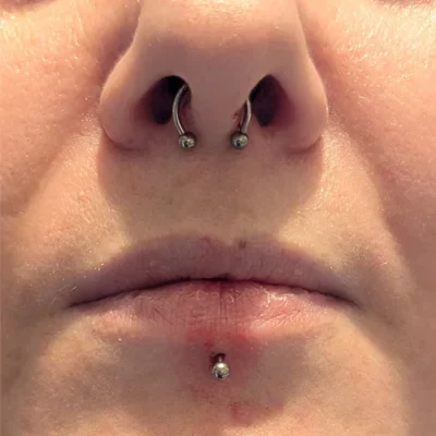 Close up of a woman's nose and lips with a septum piercing and labret piercing.